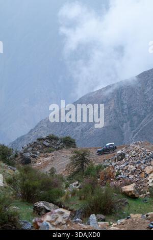 Regione di Naryn, Kirghizistan - 13 maggio 2024: Un'auto da spedizione si erge su un passo roccioso di montagna con spettacolari nuvole e nebbia sullo sfondo Foto Stock