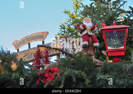 Una figura decorativa di Babbo Natale circondata da rami sempreverdi, frutti di bosco rossi, poinsettias, funghi e una lanterna rossa sul tetto di un Natale Foto Stock