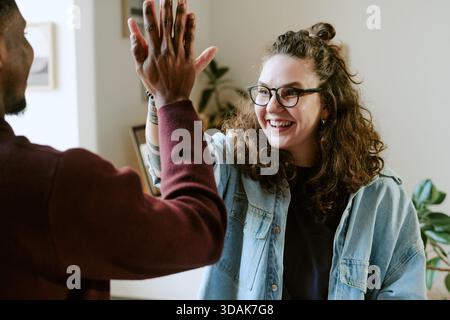 Giovane donna caucasica sorridente mentre dà High Five al giovane uomo Nero Foto Stock