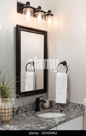 Un bagno moderno con ripiano in pietra, lavabo e armadietto bianchi, rubinetto nero e grande specchio. Foto Stock