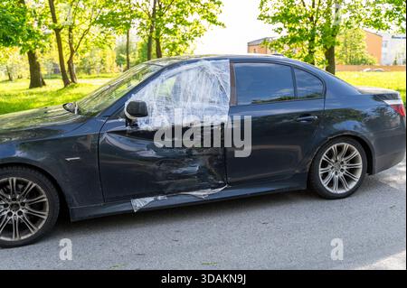 Auto parcheggiata su strada con la portiera lato conducente ammaccata e avvolta in plastica protettiva dopo l'impatto Foto Stock