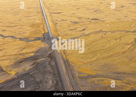 Vista aerea di una lunga strada rettilinea che attraversa le pianure autunnali dell'Islanda nord-orientale tra paesaggi vulcanici e vaste aree selvagge aperte. Foto Stock