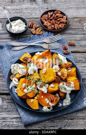 fette di zucca al forno con mozzarella, timo, noci pecan tostata, formaggio sbriciolato su un tavolo in legno rustico con forchette e panna acida, verticale Foto Stock