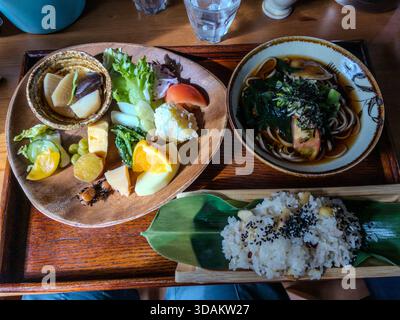 Pranzo a menu fisso giapponese, visto dall'alto: Su un vassoio di legno, riso servito su una foglia di bambù, un piatto di contorni di verdure di stagione e verdure sottaceto, e una ciotola di zuppa di soba con wakame e funghi. Ristorante a Nakatsugawa, Prefettura di Gifu, Giappone Foto Stock