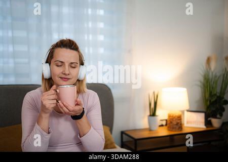 Donna che si diverte con un caffè con le cuffie e si rilassa a casa Foto Stock