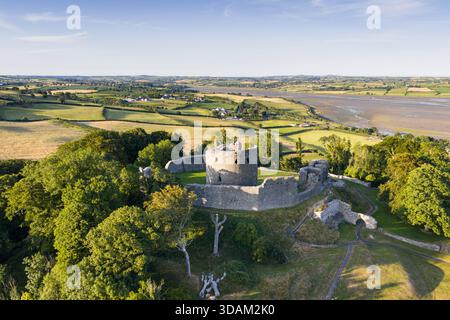 Una foto aerea panoramica di un castello medievale in rovina arroccato su una collina, circondato da lussureggianti campi, alberi e sentieri tortuosi, con una costa lontana e. Foto Stock