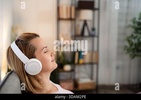 Donna che si rilassa a casa ascoltando la musica con le cuffie Foto Stock