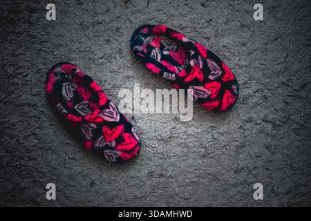 Pantofole da donna dai colori vivaci su un tappeto grigio e dalla composizione astratta. Foto Stock