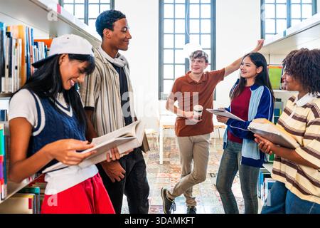 Gruppo multietnico di giovani studenti riuniti in biblioteca - giovani studenti multietnici impegnati in studio di gruppo e lavoro di squadra, in piedi tra bookshelv Foto Stock