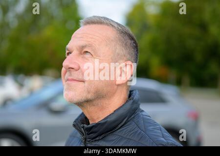 Ritratto di un uomo di mezza età con una giacca scura che guarda verso l'alto con un'espressione calma e premurosa all'aperto. Foto Stock