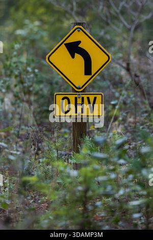 Un colpo mirato di un segnale di avvertimento giallo a forma di diamante che indica una curva sinistra acuta, abbinato a una sottopiastra che indica l'area per OHV (Off-Highwa Foto Stock