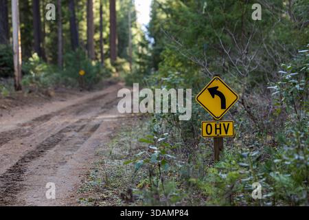 Un colpo mirato di un segnale di avvertimento giallo a forma di diamante che indica una curva sinistra acuta, abbinato a una sottopiastra che indica l'area per OHV (Off-Highwa Foto Stock