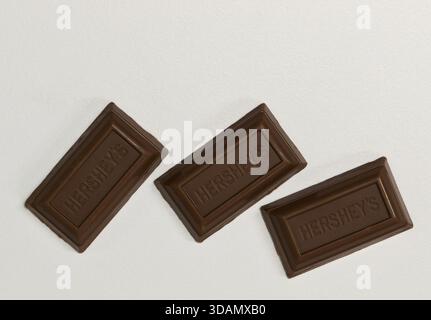 Houston, Texas Stati Uniti d'America 12-10-2025: Quadrati di cioccolato al latte a zucchero zero Hersheys sparsi su uno spazio di copia su sfondo bianco. Foto Stock