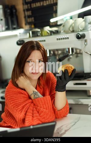 Una lavoratrice offre pasticceria dorata con guanti a mano in un moderno ambiente da caffè Foto Stock