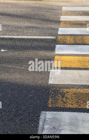 Immagine verticale di una passeggiata a strisce che mostra linee gialle e bianche che sbiadono sull'asfalto con dettagli sui bordi Foto Stock