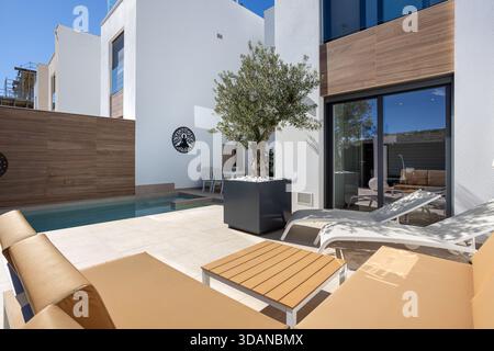 Patio luminoso e contemporaneo con lettini, piccola piscina, olivo in vaso e design minimalista Foto Stock