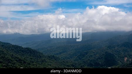 Lussureggianti montagne verdi si estendono attraverso il paesaggio sotto un cielo blu vibrante. Soffici nuvole bianche si innalzano sopra, creando un'atmosfera serena e tranquilla Foto Stock