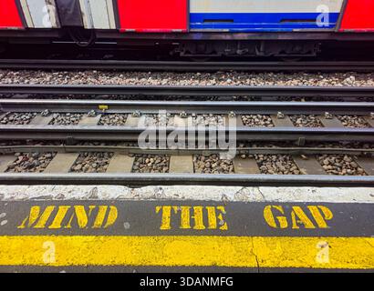 Mente gialla il testo del gap su una piattaforma della metropolitana di Londra con un treno in avvicinamento. Segnale di avvertimento della stazione della metropolitana Foto Stock