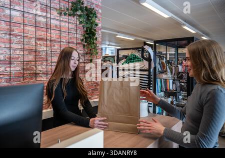 Un simpatico assistente del negozio che consegna un sacchetto di carta al cliente in un negozio di seconda mano Foto Stock