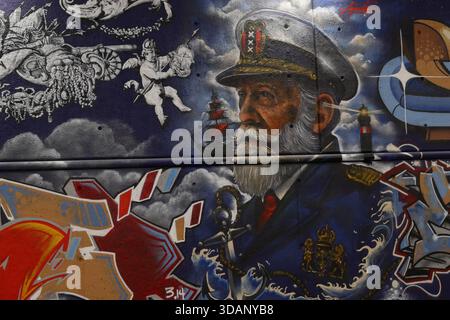 Primo piano murale con graffiti di un capitano di mare barbuto con nave e faro su un muro di sottopassaggio blu a Dijksgracht, Amsterdam, Paesi Bassi, di notte. Foto Stock