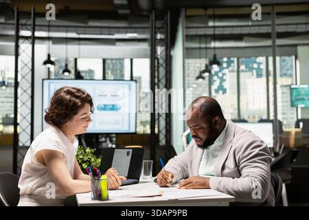 Candidato al lavoro maschile che firma il nuovo contratto di lavoro dopo essere stato accettato nell'organizzazione, professionista delle risorse umane che garantisce il processo di inserimento con documenti di lavoro e termini legali. Foto Stock