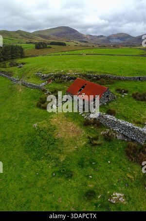 Vista aerea di un edificio in pietra abbandonato con un tetto in metallo ondulato arrugginito circondato da campi chiusi Foto Stock