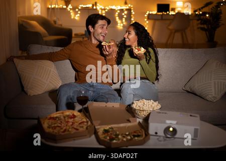 Le coppie amano la pizza e una serata di film con un proiettore nel loro accogliente soggiorno Foto Stock