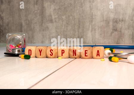 La parola DISPNEA è scritta su cubi di legno vicino ad uno stetoscopio su sfondo di legno. Concetto medico Foto Stock