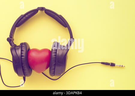 Cuffie nere con cuore rosso, fili e presa su sfondo giallo Foto Stock