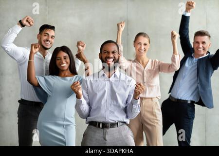 I colleghi multirazziali celebrano i risultati ottenuti con Fists sollevati in un ambiente di squadra di successo Foto Stock