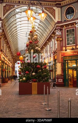 Un grande albero di Natale decorato con baubles e luci rosse e dorate sorge al centro di uno storico mercato, con gli amanti dello shopping che camminano. Foto Stock