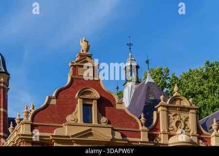 Vista dettagliata della facciata superiore di un edificio ornato in stile vittoriano, che mostra intricati mattoni rossi, elementi in stucco gialli e una cupola prominente Foto Stock