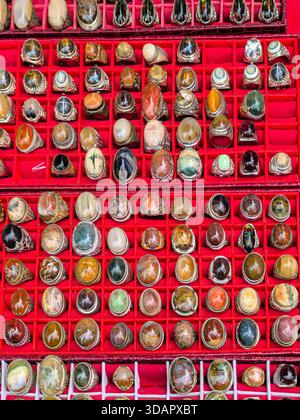 IPOH, MALESIA - 09 NOVEMBRE 2025: Una vista dall'alto di vari anelli con grandi agate e pietre preziose esposte in un vassoio scanalato rosso Foto Stock