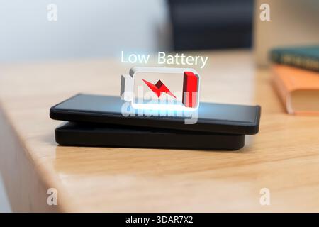 Un'icona di avviso di batteria scarica proiettata sopra uno smartphone posizionato su un caricabatterie wireless, che rappresenta mancanza di alimentazione, esaurimento della batteria e utilizzo del dispositivo digitale Foto Stock