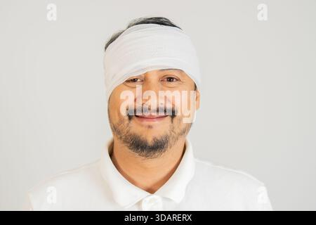 Ritratto ravvicinato di un uomo asiatico sorridente con bendaggio sulla testa su sfondo bianco. Immagine correlata al trattamento delle ferite Foto Stock