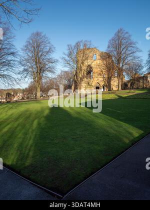 Lunghe ombre sparse attraverso i verdi giardini del castello con le rovine del castello di Knaresborough sullo sfondo. Foto Stock