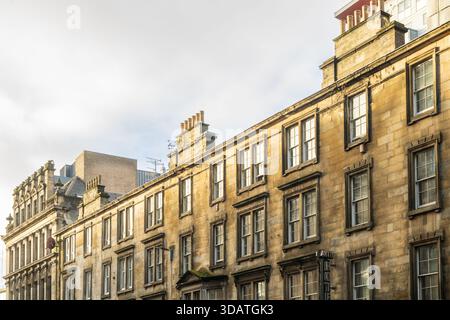 Vista degli edifici in pietra invecchiati che si crogiolano nel caldo bagliore del sole pomeridiano, le loro finestre riflettono la luce soffusa, creando una scena urbana senza tempo, Foto Stock