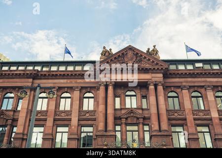 Veduta di un edificio in mattoni rossi con finestre ad arco, statue e bandiere blu che fluttuano contro un cielo parzialmente nuvoloso, Brema, Brema, Germania. Foto Stock