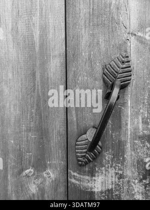 Maniglia per mobili forgiata su una vecchia porta in legno malandato. Stile retrò. Copia spazio. Primo piano. Foto in bianco e nero. Foto Stock