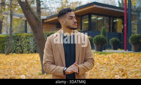 Un uomo ispanico preoccupato nel parco autunnale guardati intorno in attesa di un incontro alla ricerca di un'attesa delusa nervosa triste uomo in piedi all'aperto in autunno Foto Stock