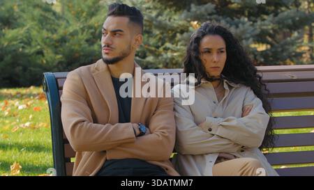 Stressata coppia ispanica ignorando sentimento offeso sulla panchina nel parco autunnale famiglia negativa silenzioso ignorare la separazione uomo arabo con donna caucasica Foto Stock