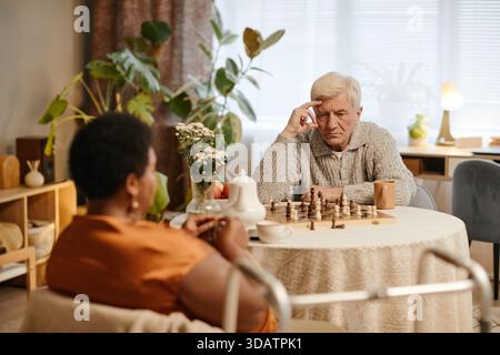 Senior Caucasian Man si concentra mentre gioca a scacchi con Senior Black Woman Foto Stock