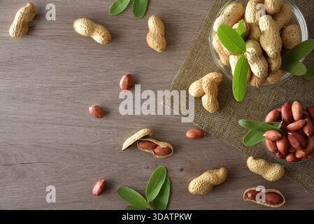 Arachidi sbucciate e non sbucciate in ciotole di vetro su una panca di legno da cucina. Vista dall'alto. Foto Stock