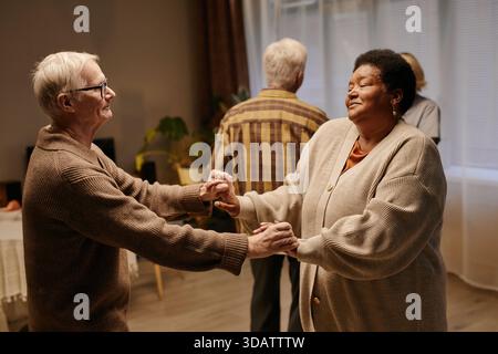 Uomo caucasico anziano e donna nera anziana che si tengono per mano e ballano insieme Foto Stock