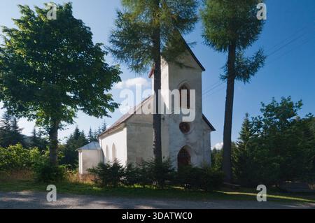 Vista di una pittoresca chiesa bianca annidata tra alberi verdeggianti sotto un cielo azzurro e limpido, un luogo di culto tranquillo, Magurka, Zilinský kraj, Slovacchia. Foto Stock