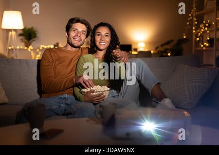La coppia felice si diverte a vedere film a casa con Popcorn e proiettore Foto Stock