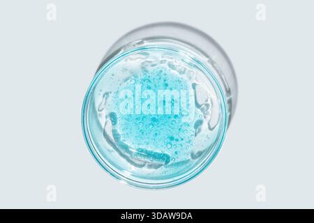 Vista dall'alto di una consistenza di gel blu brillante all'interno di vetreria da laboratorio trasparente. Le bolle trasparenti e la superficie liscia del gel contrastano Foto Stock