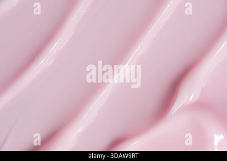 Immagine ravvicinata di una texture cosmetica fluida e fluida in una tenue tonalità rosa. La sostanza cremosa è ricoperta da curve delicate che creano una delicata cal Foto Stock