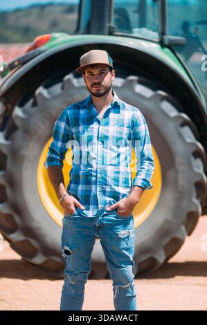 Un agricoltore si trova di fronte a un grande trattore in una giornata di sole a Guadalajara, in Spagna, mostrando la dedizione e lo spirito dell'agricoltura moderna Foto Stock