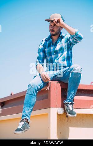 Un contadino in abbigliamento casual, seduto su un rimorchio a Guadalajara, Spagna. Il cielo blu e la postura rilassata evidenziano un sereno stile di vita rurale in mezzo al Foto Stock